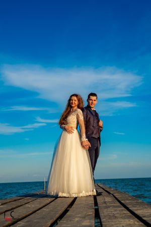 Romantic wedding portrait captured on a wooden dock against vibrant blue ocean backdrop.
