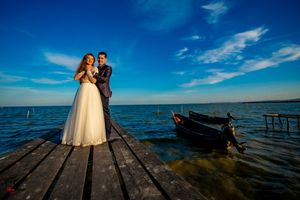 Wedding couple stands on a wooden pier overlooking a serene blue ocean under bright summer skies.