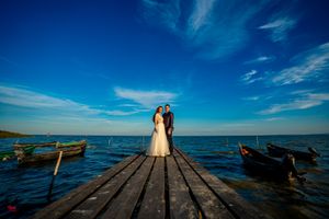 Panoramic view of couple in wedding attire on wooden pier over ocean waters.