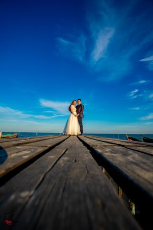 Low angle view of wedding couple on wooden pier against bright blue sky.