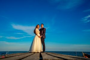 Newlyweds share a moment on oceanfront pier under bright blue skies.