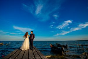 Wide angle shot of a wedding couple on a wooden pier with dramatic blue sky and ocean view.