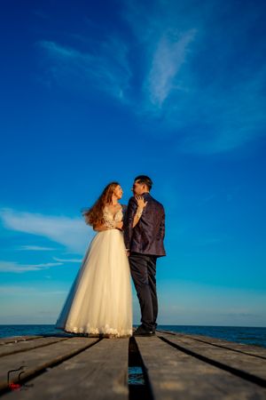 A couple sharing an intimate moment on a wooden pier against a vibrant blue sky.