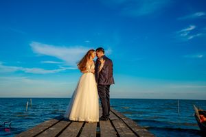 A romantic moment captured on a wooden dock with the ocean and boats in the background.