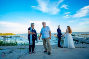 People conversing on a concrete pier overlooking a scenic waterfront with boats in the distance.