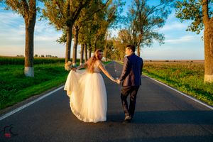 A couple walks together on a tree-lined country road during their wedding photoshoot.