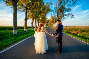 A couple holds hands while standing on a rural road lined with autumn trees.