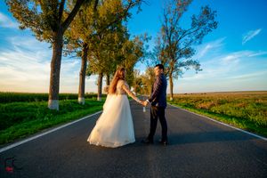 A couple shares a romantic moment on a tree-lined road during their wedding photoshoot.