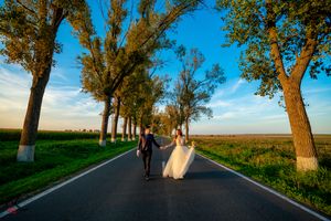 A couple walks together on a rural road lined with tall trees during golden hour.