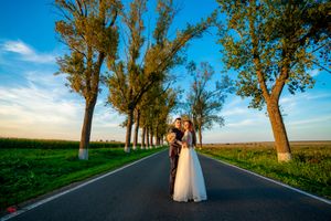 Wedding couple poses along rural road with rows of tall trees creating natural archway.