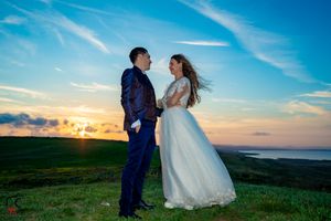 Dramatic sky and flowing dress create romantic wedding scene on windswept hilltop.