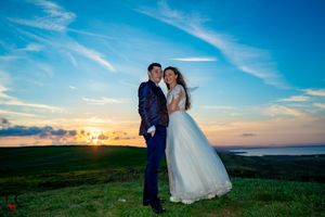 Elegant wedding portrait on a grassy hill with dramatic clouds and sunset lighting.
