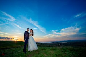 Romantic sunset wedding photo with couple standing on scenic hilltop overlook.