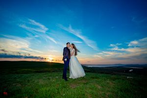 Wedding couple embraces on rolling hills during golden hour with panoramic countryside views.