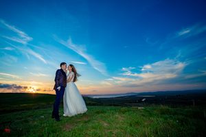 Newlyweds stand together on a grassy hillside with sweeping views and blue skies.