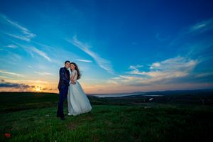 Wedding photography session at sunset showcases couple against dramatic sky and rolling hills.