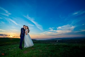 Wedding couple poses against dramatic evening sky on scenic hilltop location.