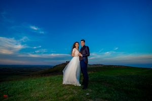 Bride and groom share intimate moment on hilltop with spectacular sunset backdrop.