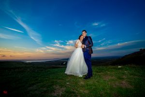 Wedding portrait captured on rolling green hills with stunning dusk sky and mountain backdrop.