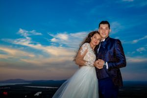 Wedding couple embraces on grassy hillside during golden hour with dramatic sky in background.