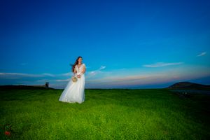 Panoramic wedding photo with couple in distance on bright green hilltop meadow.