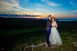 Sunset wedding photography with couple standing on green hillside overlooking ocean.