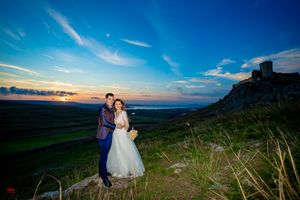 Wedding couple poses on scenic overlook with dramatic sky and rolling hills.