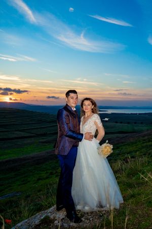 Elegant wedding portrait with couple embracing on hilltop during golden hour.