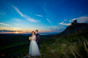 Panoramic wedding photo with couple against stunning coastal sunset and mountain backdrop.