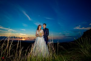 Wedding couple silhouetted against dramatic sunset sky with rolling hills and ocean views.