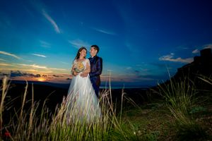 Wedding couple stands against panoramic mountain vista at twilight.
