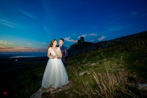 Wedding couple stands among tall grass with mountain backdrop at golden hour.