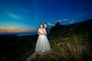 Newlyweds embrace on hilltop with sweeping mountain views at sunset.