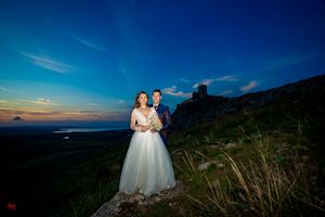Romantic wedding portrait silhouetted against vibrant blue mountain sky at dusk.