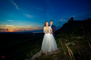 Romantic wedding portrait at dusk with mountain castle and sunset sky.
