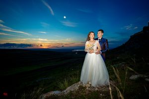 Sunset wedding photo with couple standing on rocky outcrop against colorful sky.