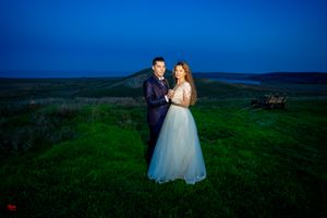 Wedding portrait with dramatic lighting on a grassy hill at dusk.