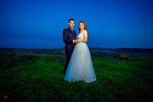 Elegant wedding couple embraces on green hillside during evening photography session.