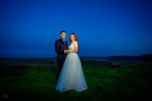 A romantic wedding portrait captured on a hilltop with vibrant blue sky backdrop.