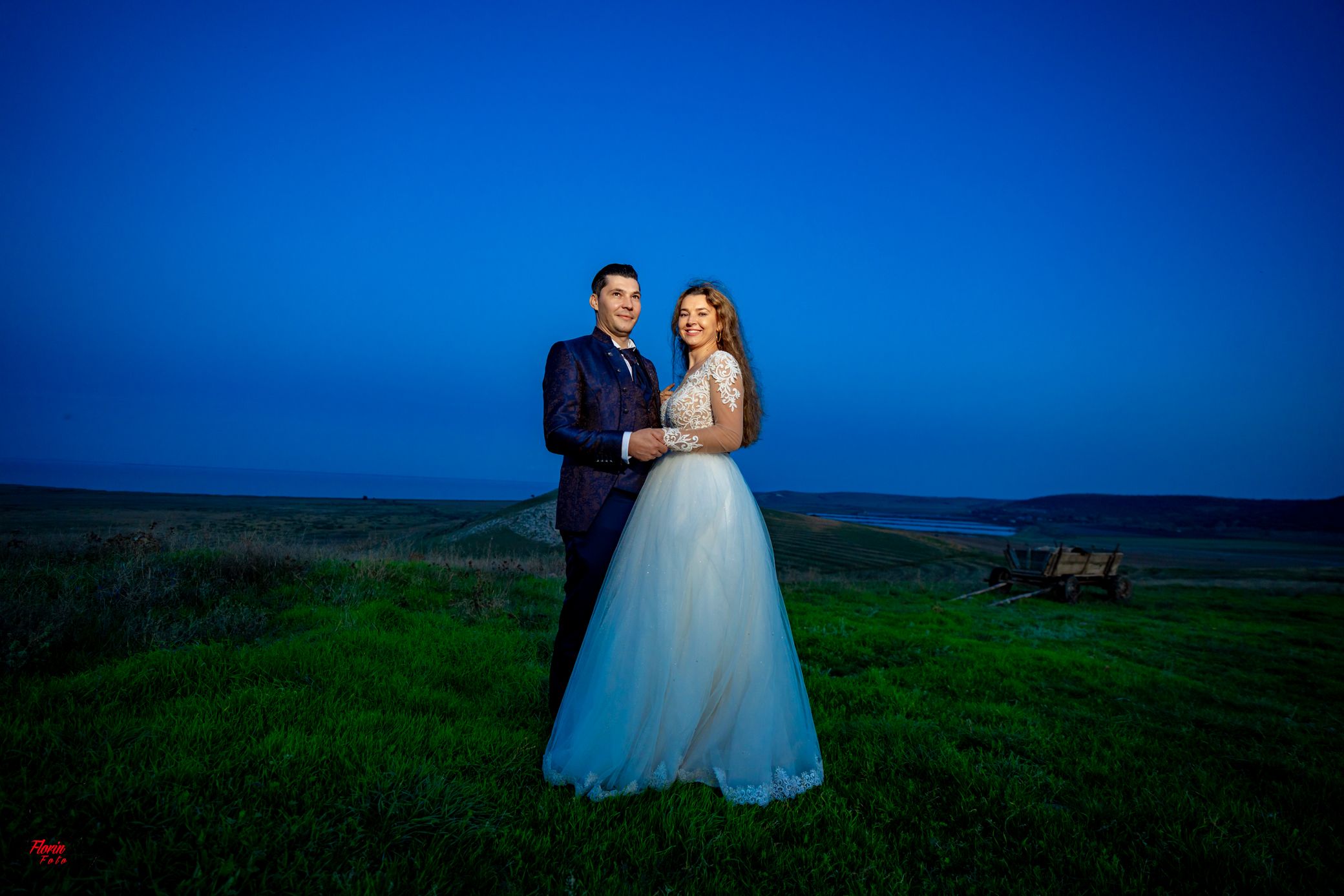 Newlyweds pose together on a hillside during blue hour with dramatic lighting.