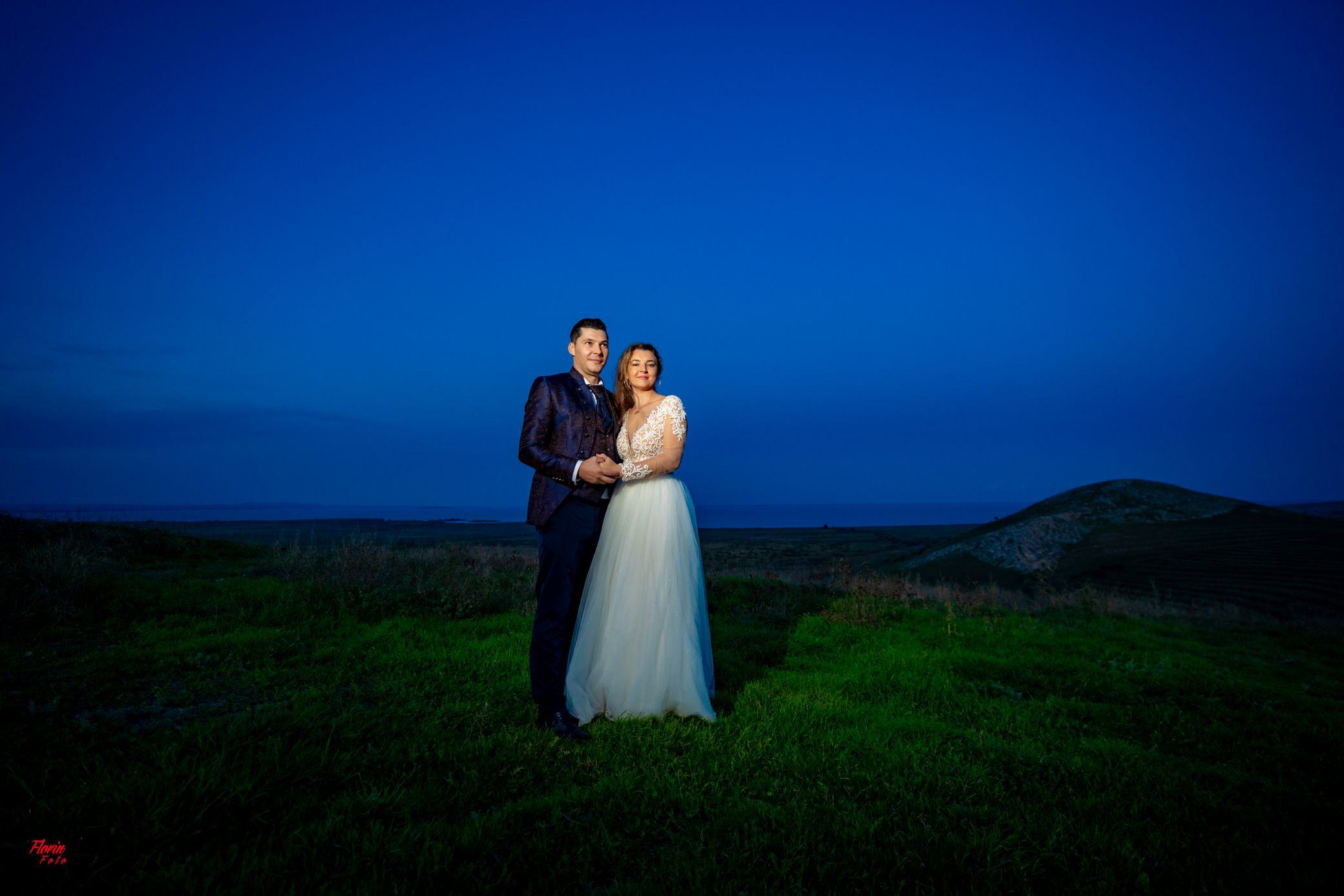 Couple's silhouette against deep blue evening sky in pastoral setting.