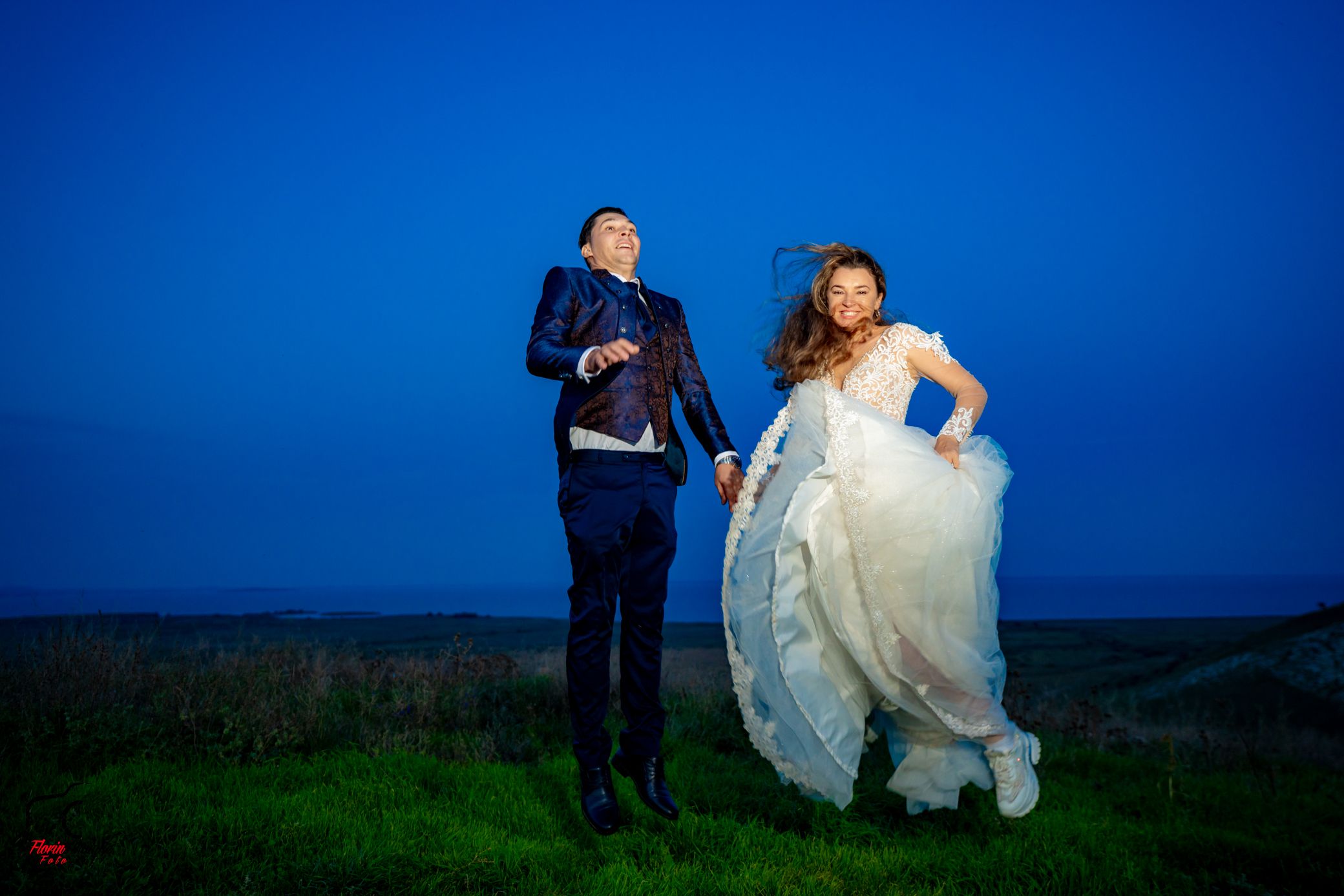 Newlyweds share intimate moment against vibrant blue sky in rural landscape.