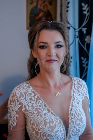 Close-up portrait of a bride wearing an elegant lace wedding dress with sheer sleeves and intricate beading details.