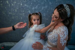 Candid moment during a wedding photoshoot with matching white dresses against a blue backdrop.