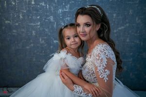 Elegant wedding photo featuring matching white dresses against a textured blue wall background.