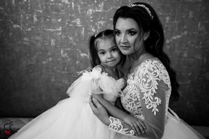 Black and white portrait showing a sweet embrace between a bride and young girl in matching white dresses.
