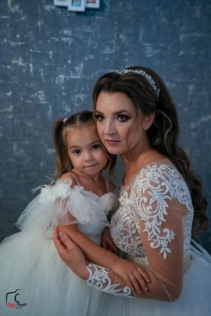 Intimate portrait of a bride and young girl in matching white dresses against a moody blue backdrop.