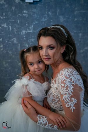 A tender moment captured between a bride in lace and a young girl in a white tulle dress against a blue textured wall.