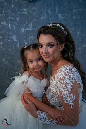 Intimate portrait of bride and flower girl embracing during wedding photoshoot.