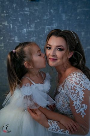Sweet candid moment between bride and flower girl against blue textured backdrop.